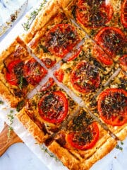 Sliced tomato tart on a wooden cutting board with a knife.