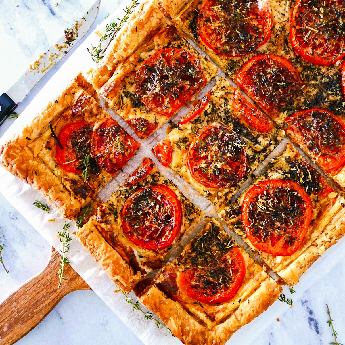 Sliced tomato tart on a wooden cutting board with a knife.