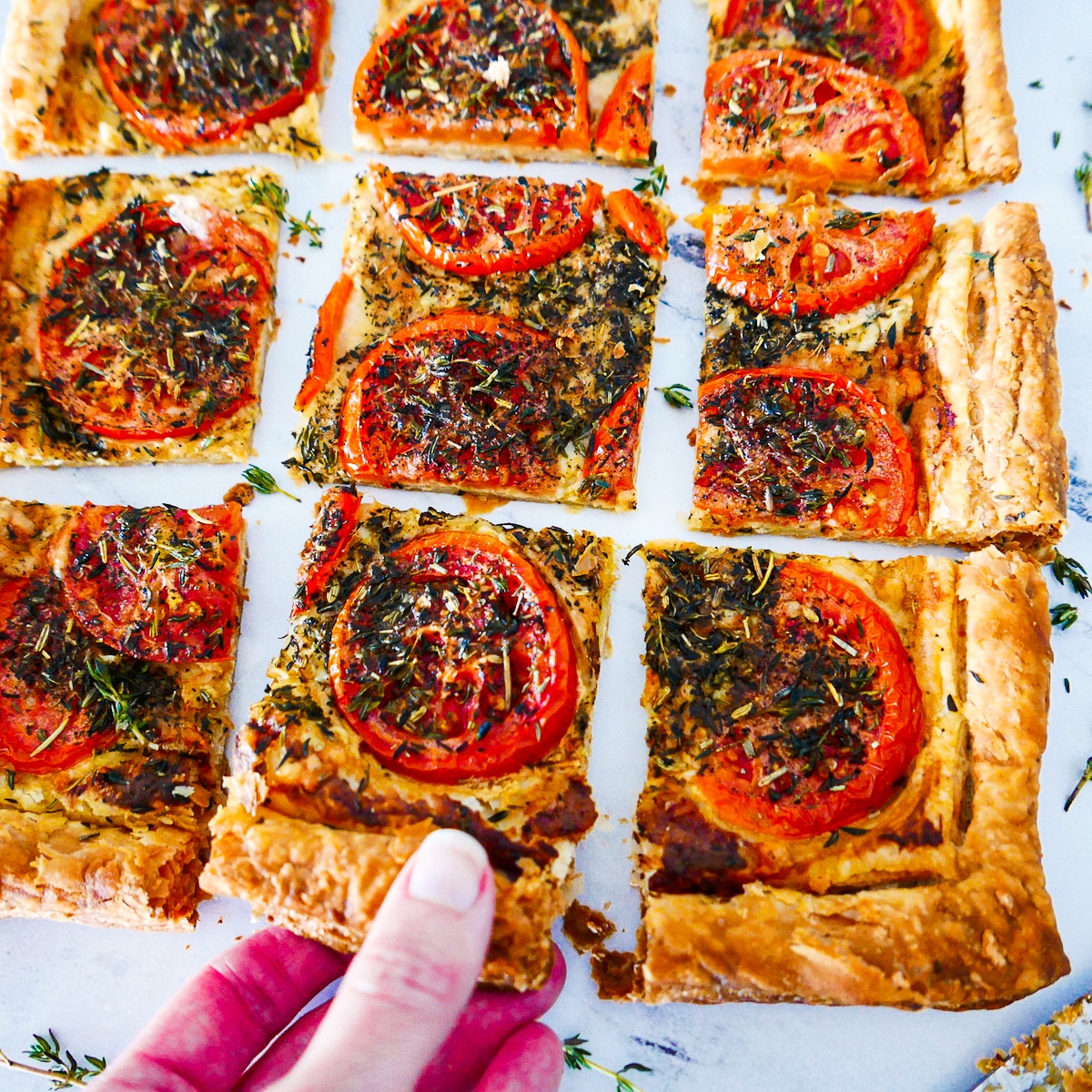 picking-up-slice-of-tart.jpg Hand picking up slice of tomato tart from a cutting board.