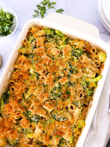 Broccoli pasta bake with plates, parsley, serving spoon, and a white napkin.