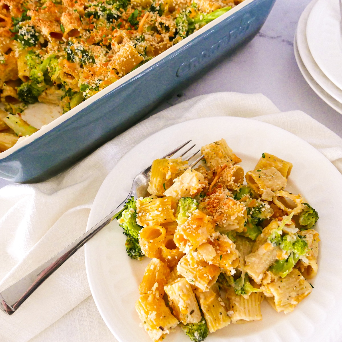 Pasta on a white plate and baking dish with two forks and white napkin.