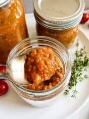 Spoonful of roasted cherry tomato sauce being lifted out of a jar.