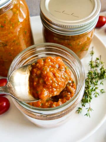 Spoonful of roasted cherry tomato sauce being lifted out of a jar.