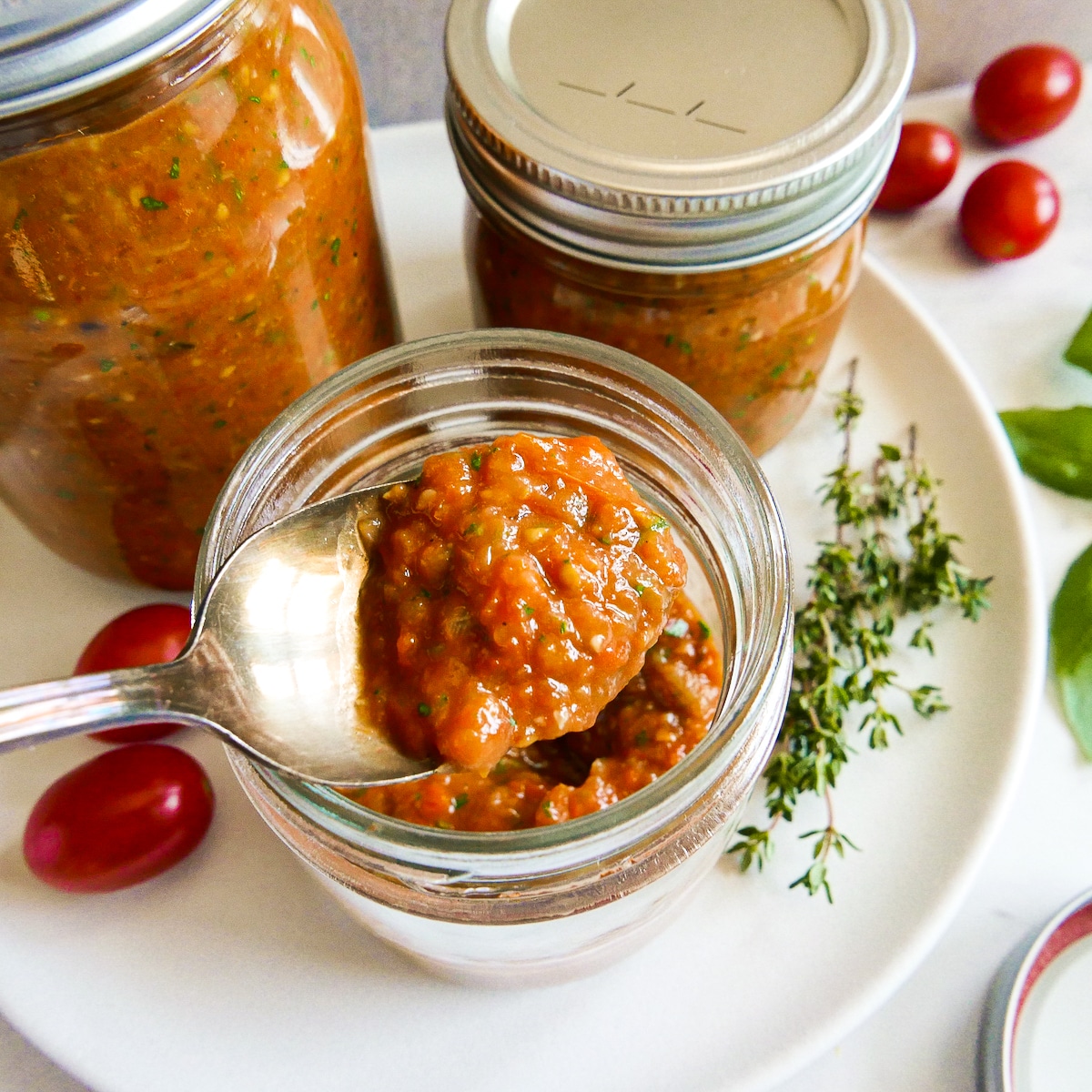 Spoonful of roasted cherry tomato sauce being lifted out of a jar.