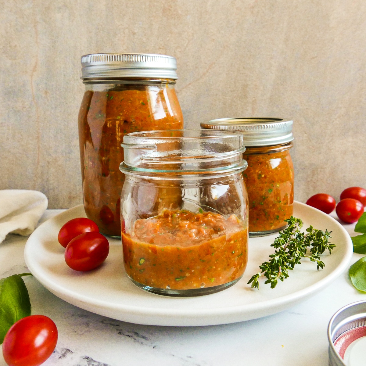 Three jars of homemade cherry tomato sauce arranged on a table.