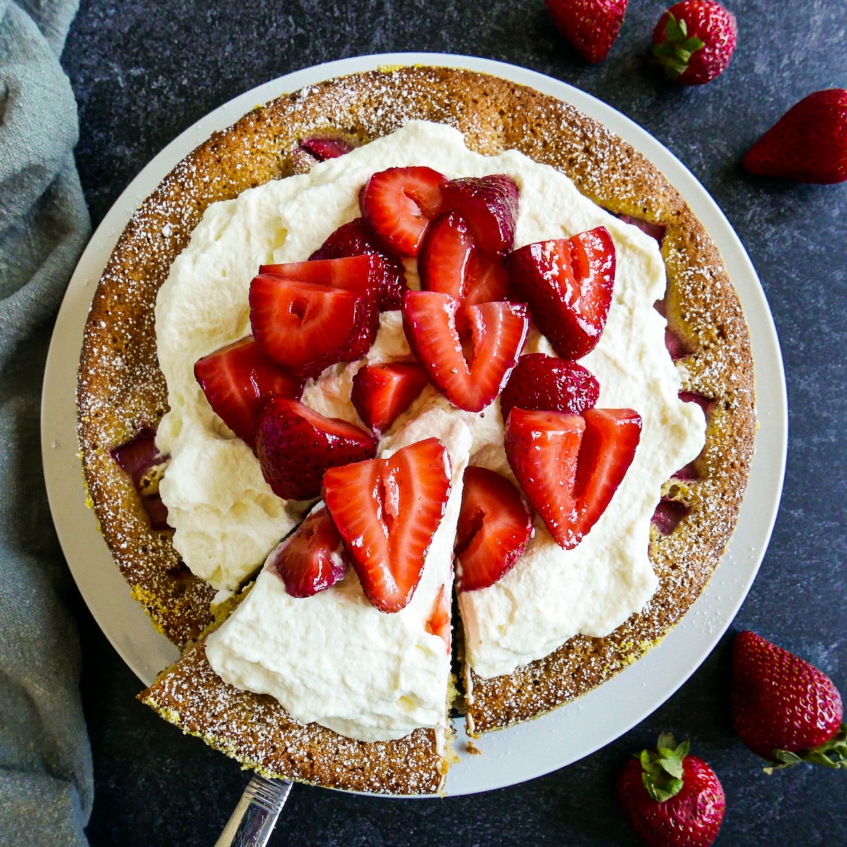 Strawberry cake topped with whipped cream and strawberries on a platter.