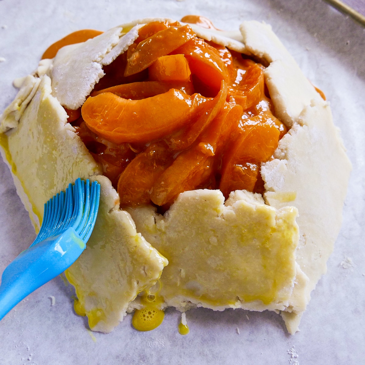 Brushing egg wash on galette dough with a pastry brush.