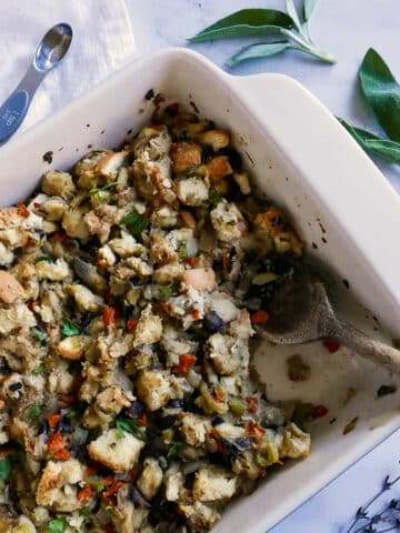 Mushroom dressing in a baking dish with a wooden spoon and sage next to dish.