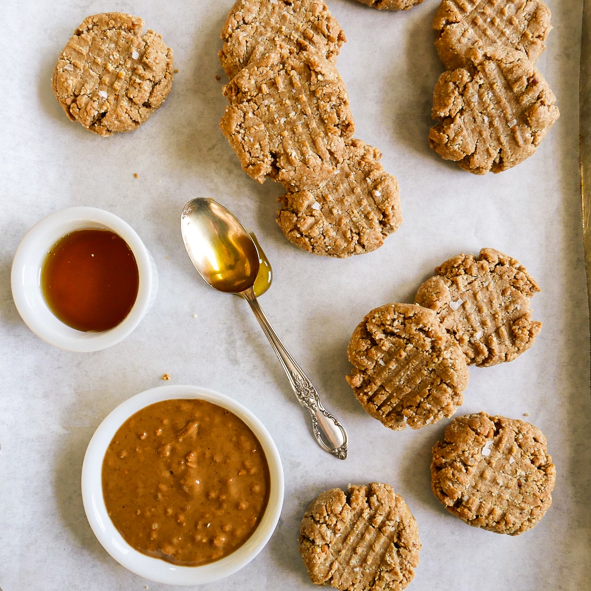 Peanut butter cookies arranged on a baking sheet with spoonful of maple syrup.