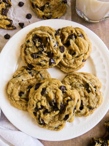 white plate with five dairy free chocolate chip cookies and a glass of milk in background.