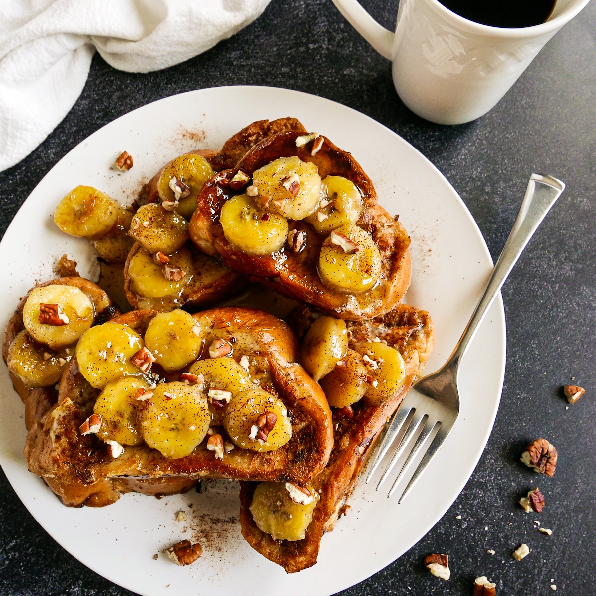 Bananas foster french toast arranged on a large plate with a fork.