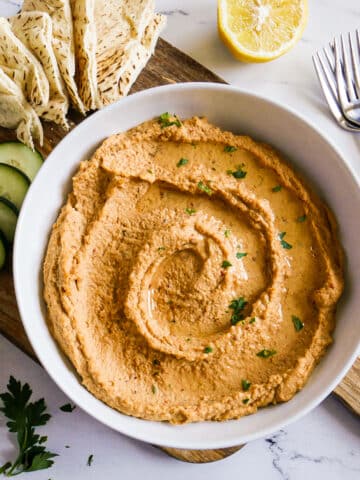 Bowl of spicy hummus garnished with fresh parsley.