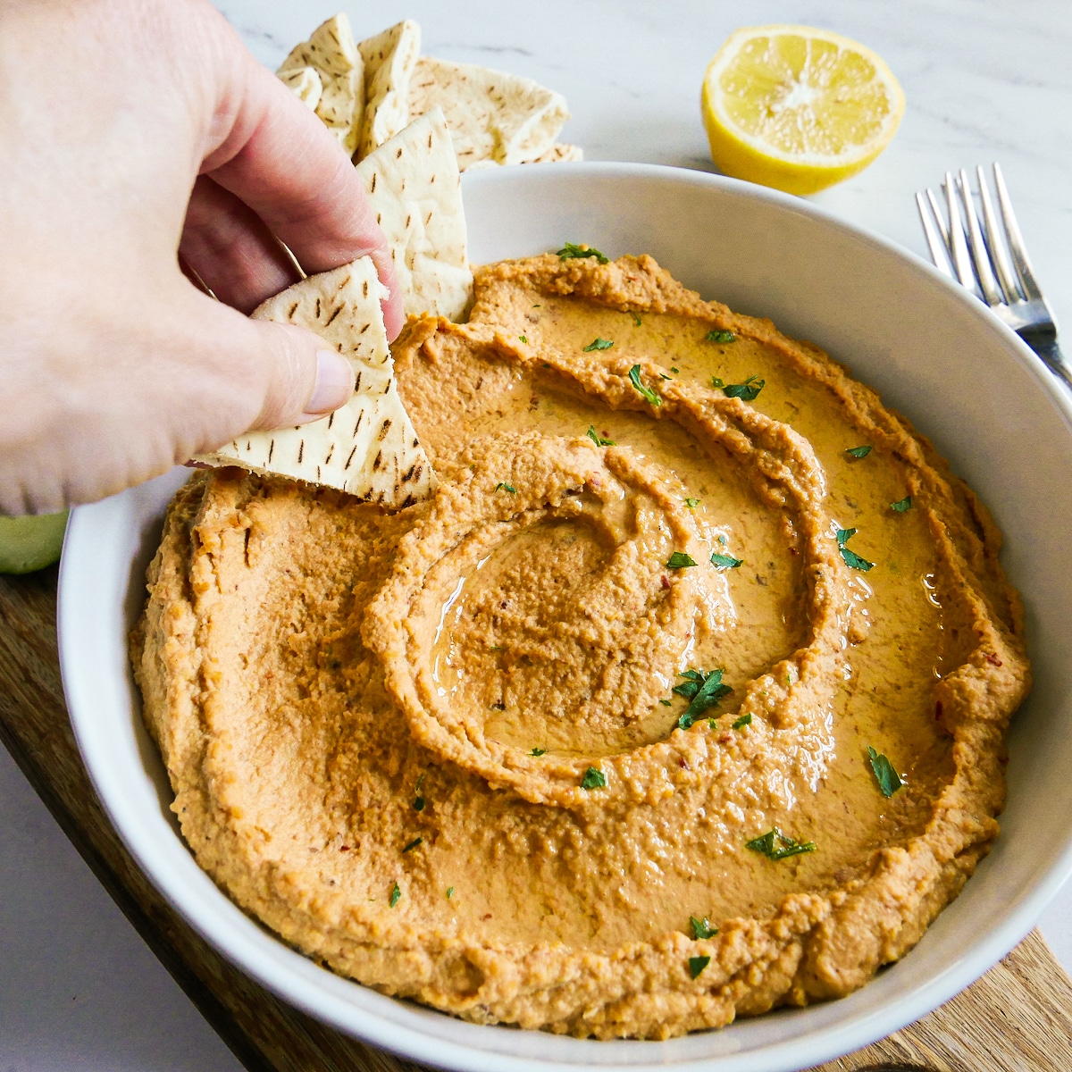 Dipping a pita chip into a large bowl of homemade hummus.