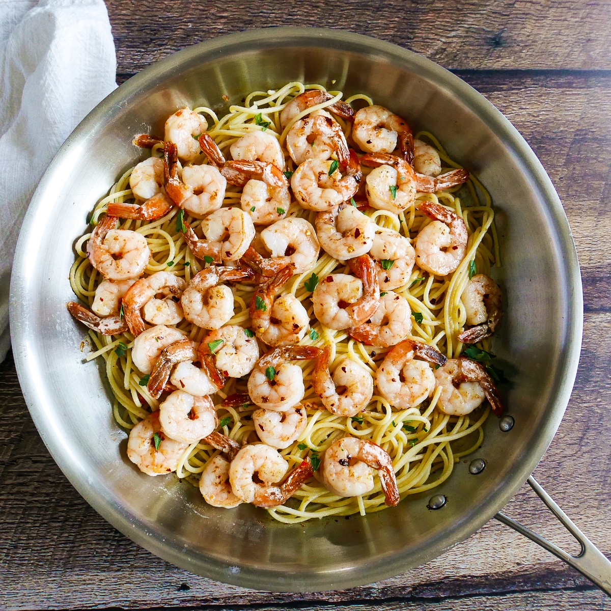 Assembled shrimp pasta in a large skillet with tongs.