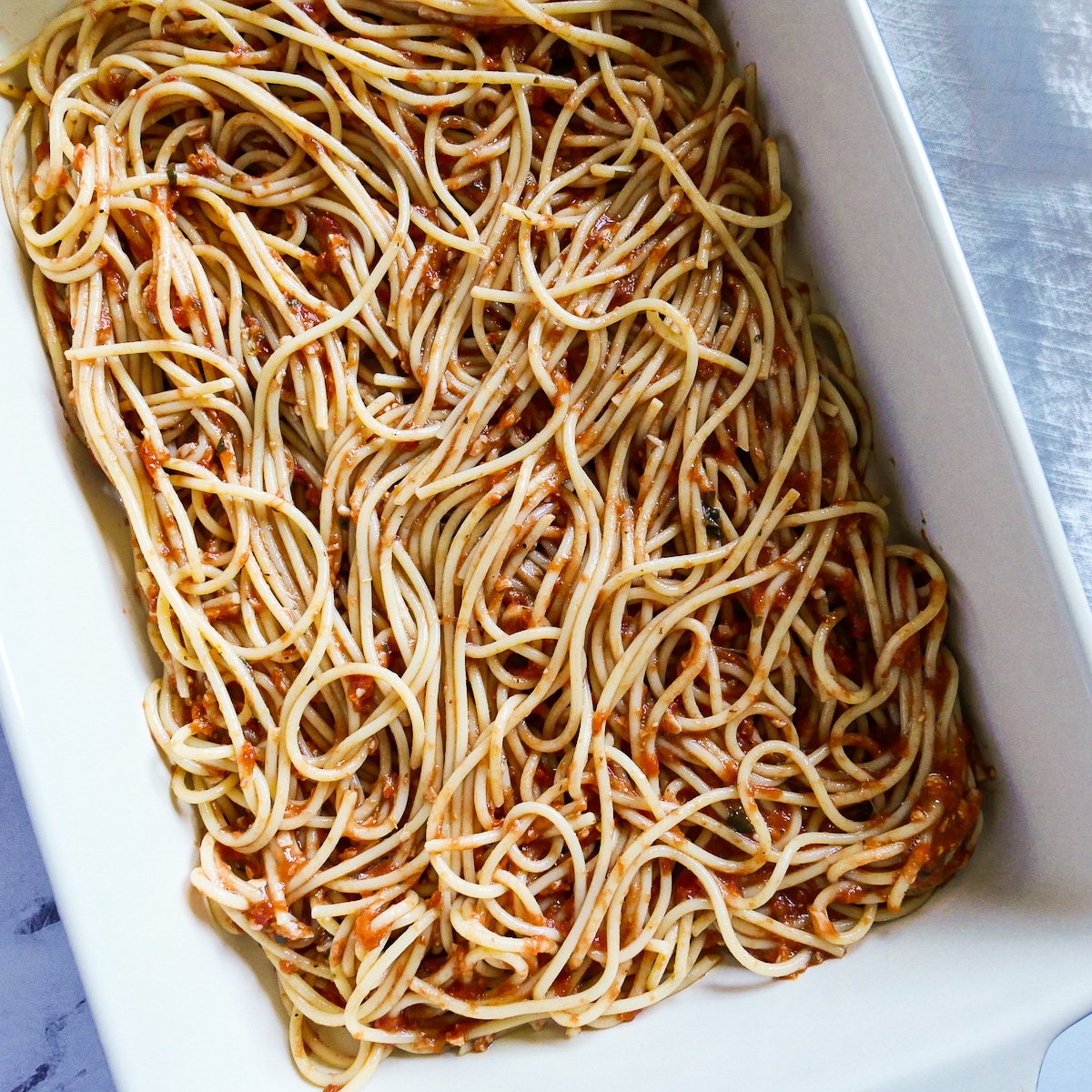 Spaghetti bake ingredients spread into a prepared baking dish.