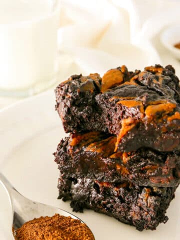 vegan pumpkin brownies stacked on a white plate with a spoon of cinnamon.