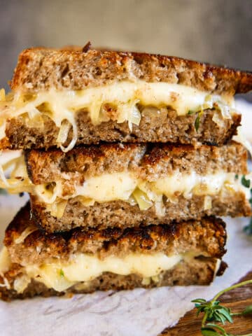 Stacked caramelized onion grilled cheese on a cutting board lined with parchment paper.