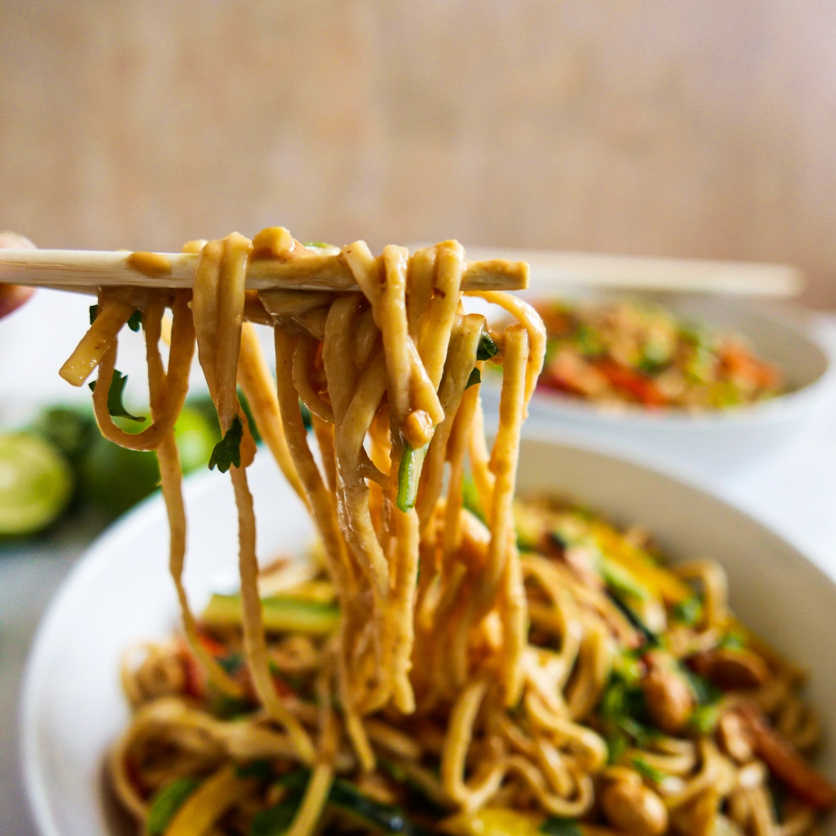 Chopsticks holding up spicy peanut noodles from bowl.