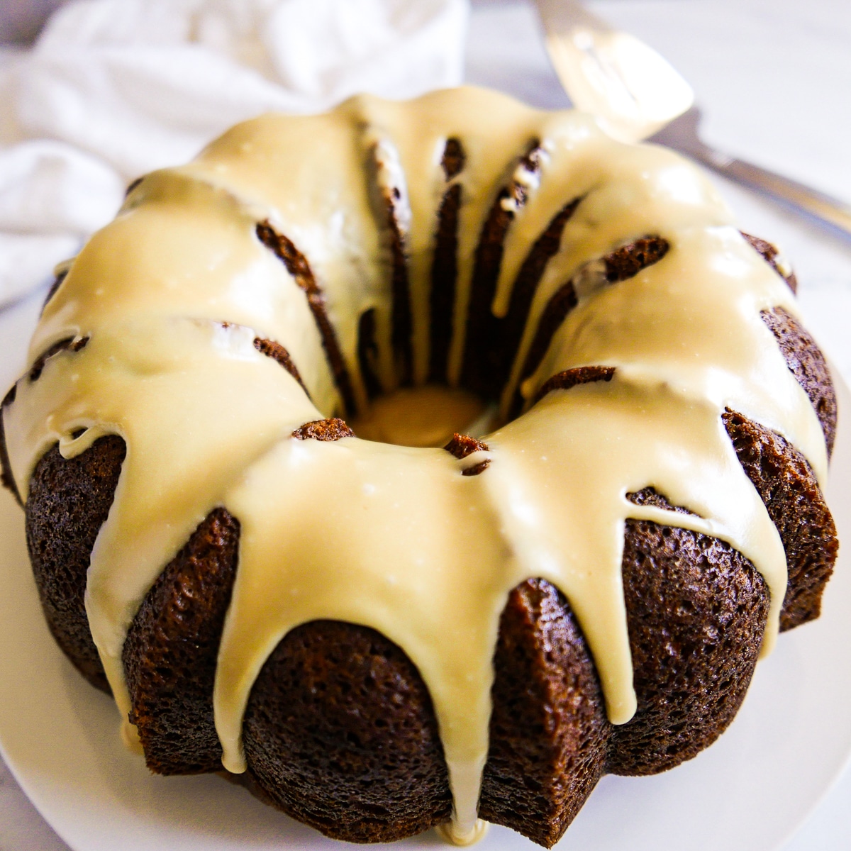 frosted spice cake on a platter with a cake server in the background. 