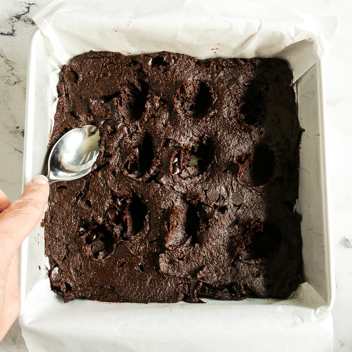 Using the back of a spoon to make indentations into brownie batter.