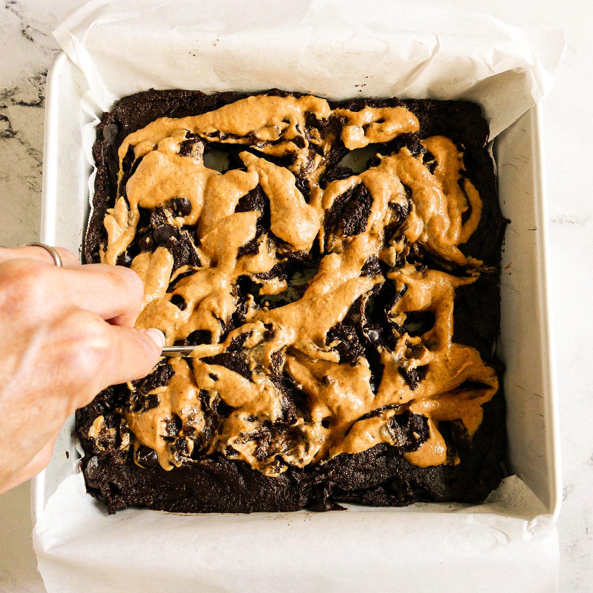 Using a spoon handle to swirl pumpkin mixture into brownie batter.