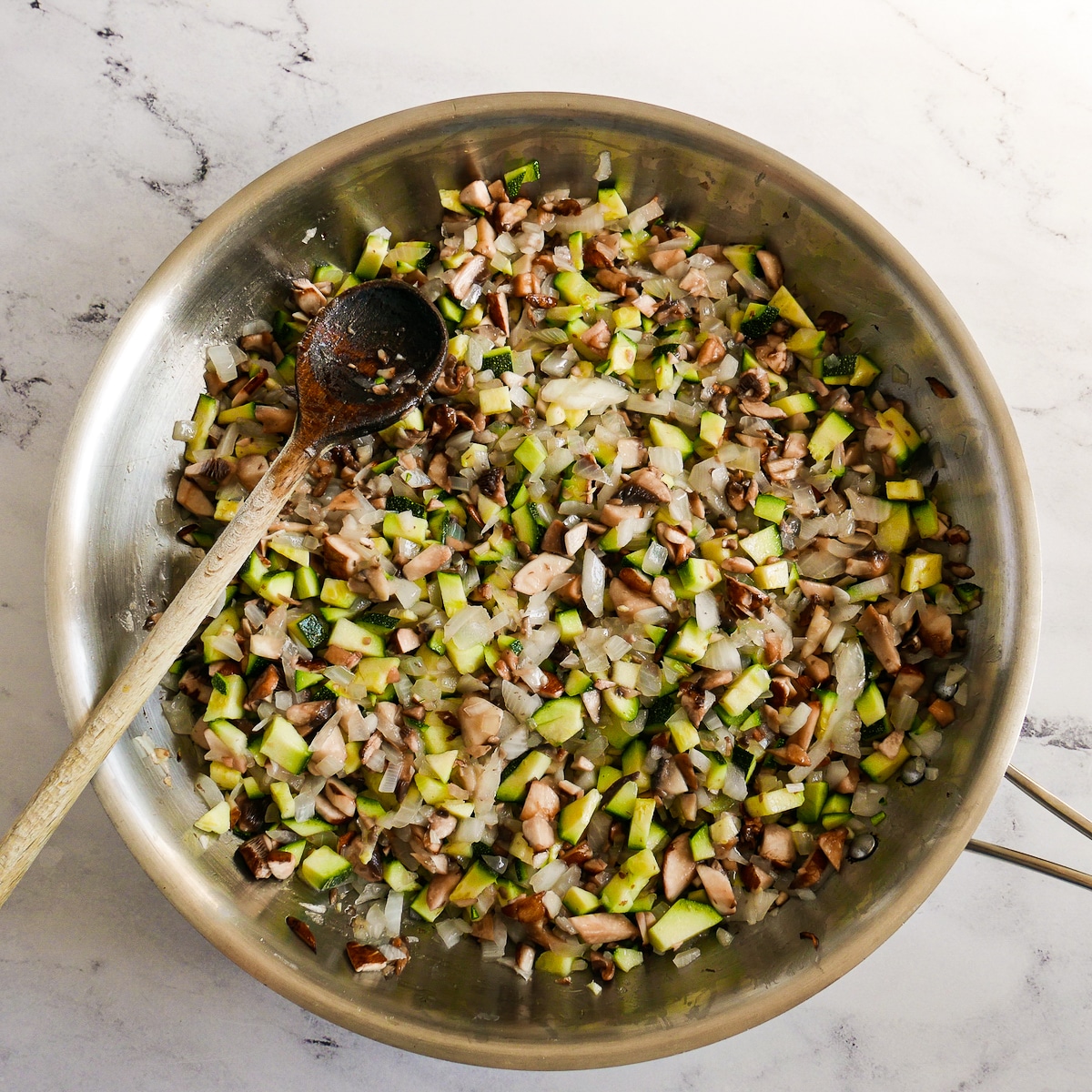 Onion, mushrooms, and zucchini cooking in a large skillet.