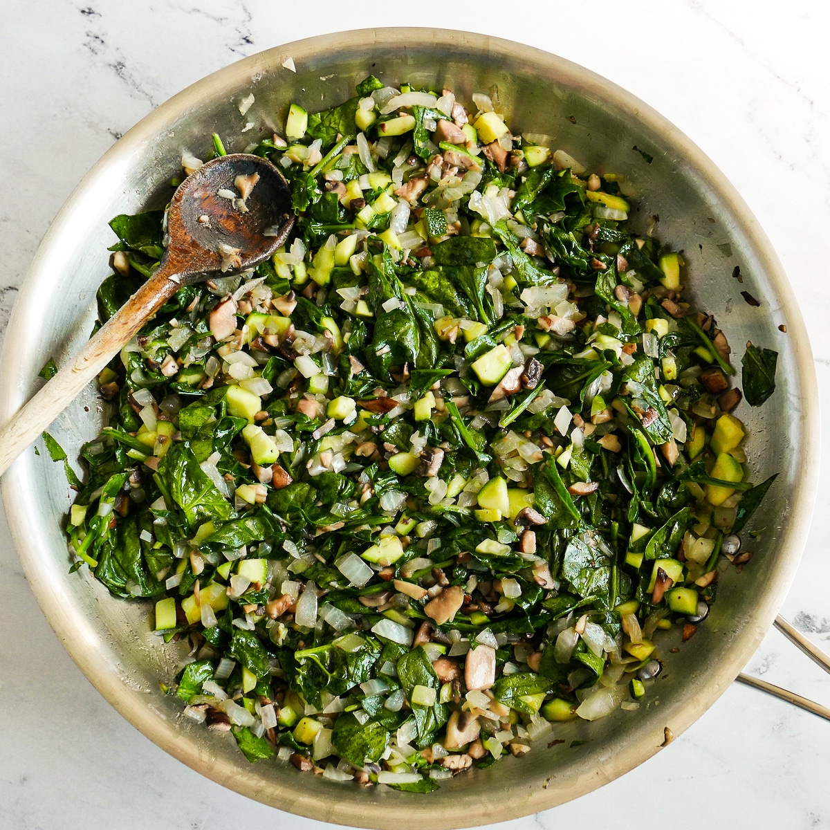 Spinach added to cooked vegetables in a skillet.