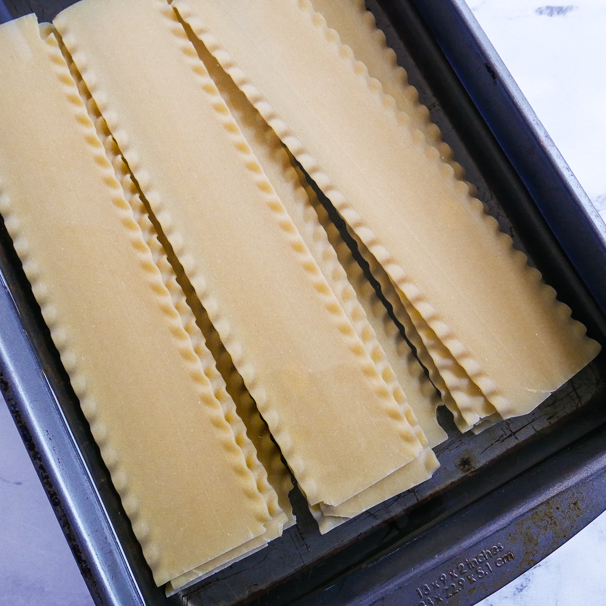 Lasagna noodles soaking in a pan of hot water.