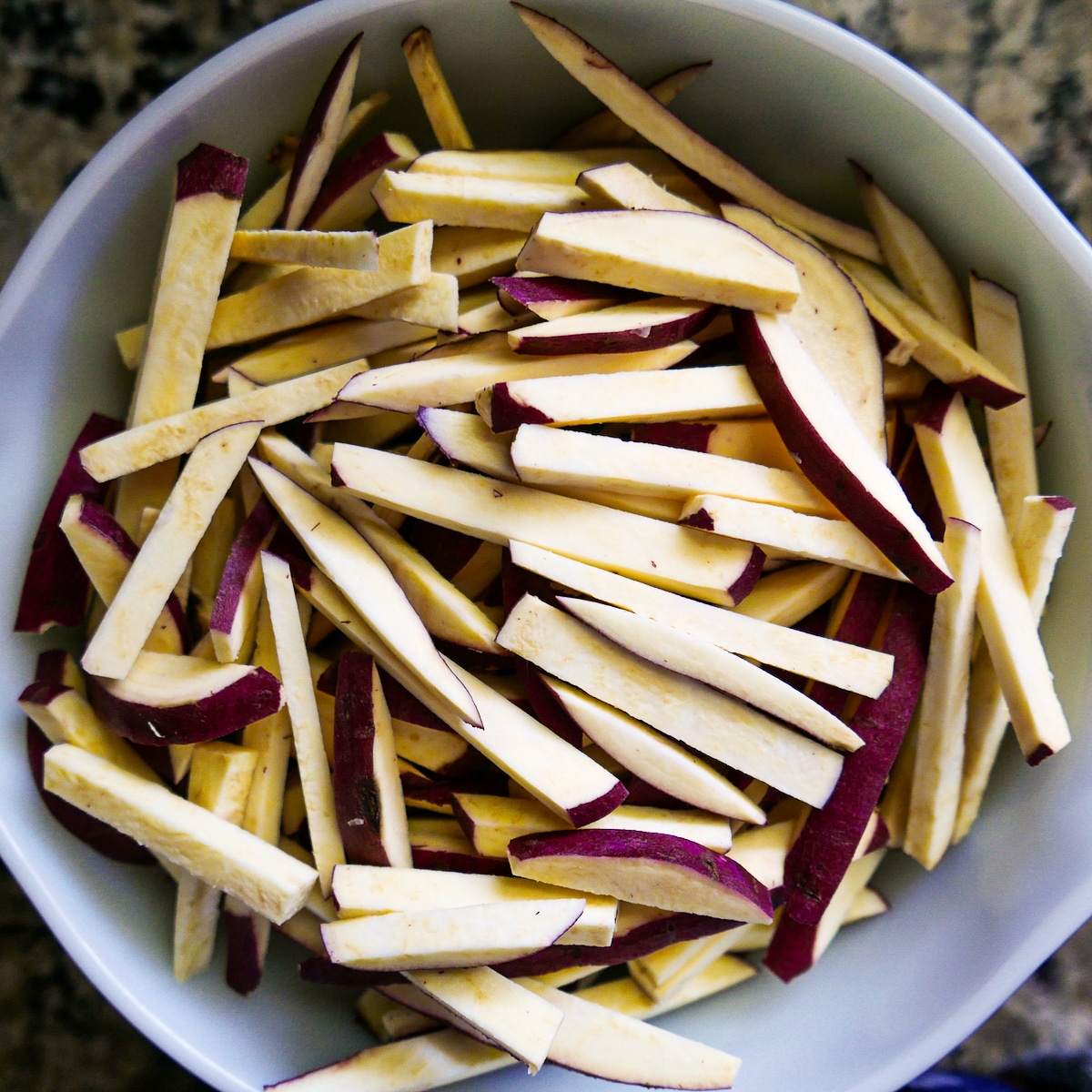 Cut sweet potatoes tossed in oil and spices in a mixing bowl.