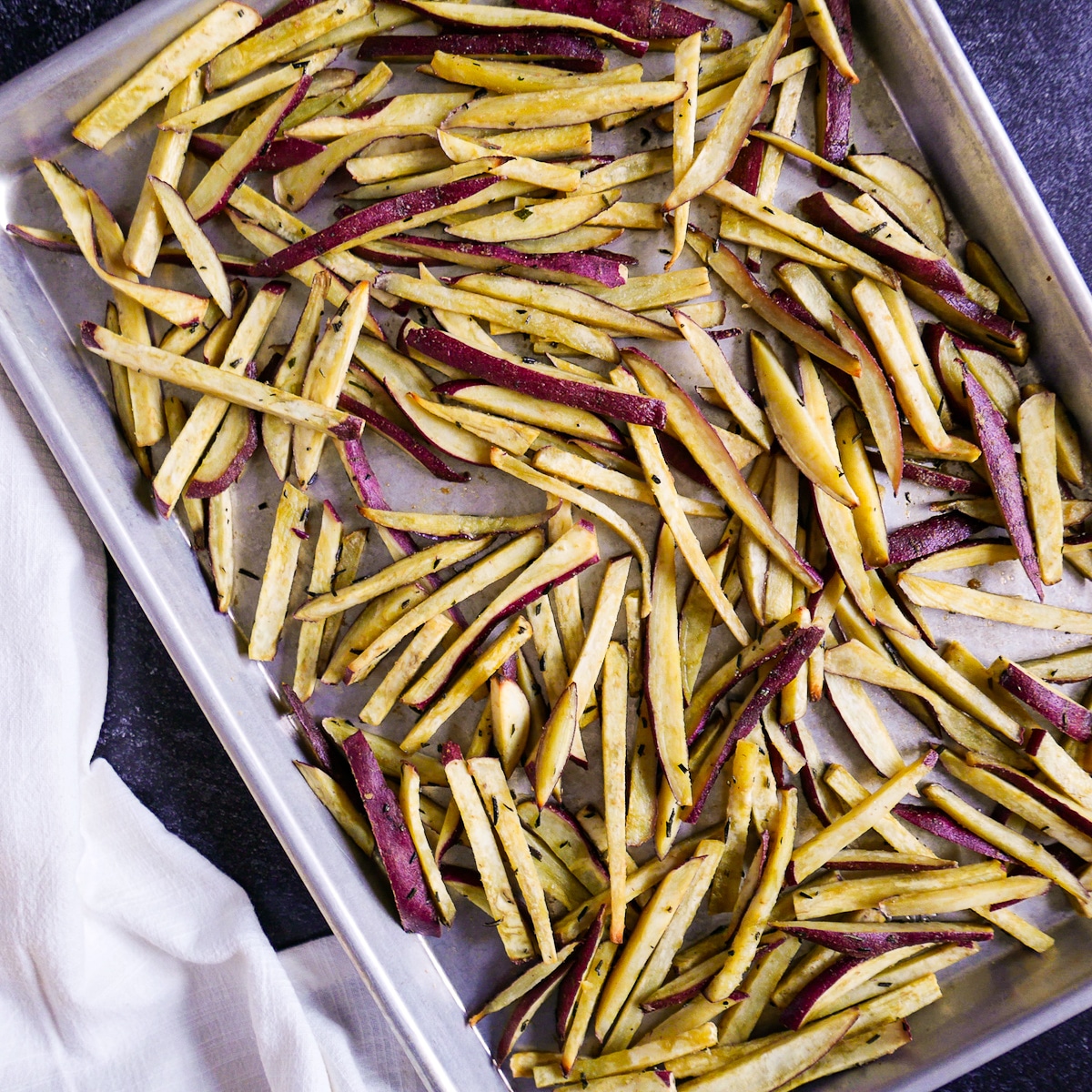 Baked sweet potato fries on a baking sheet with a napkin next to it.