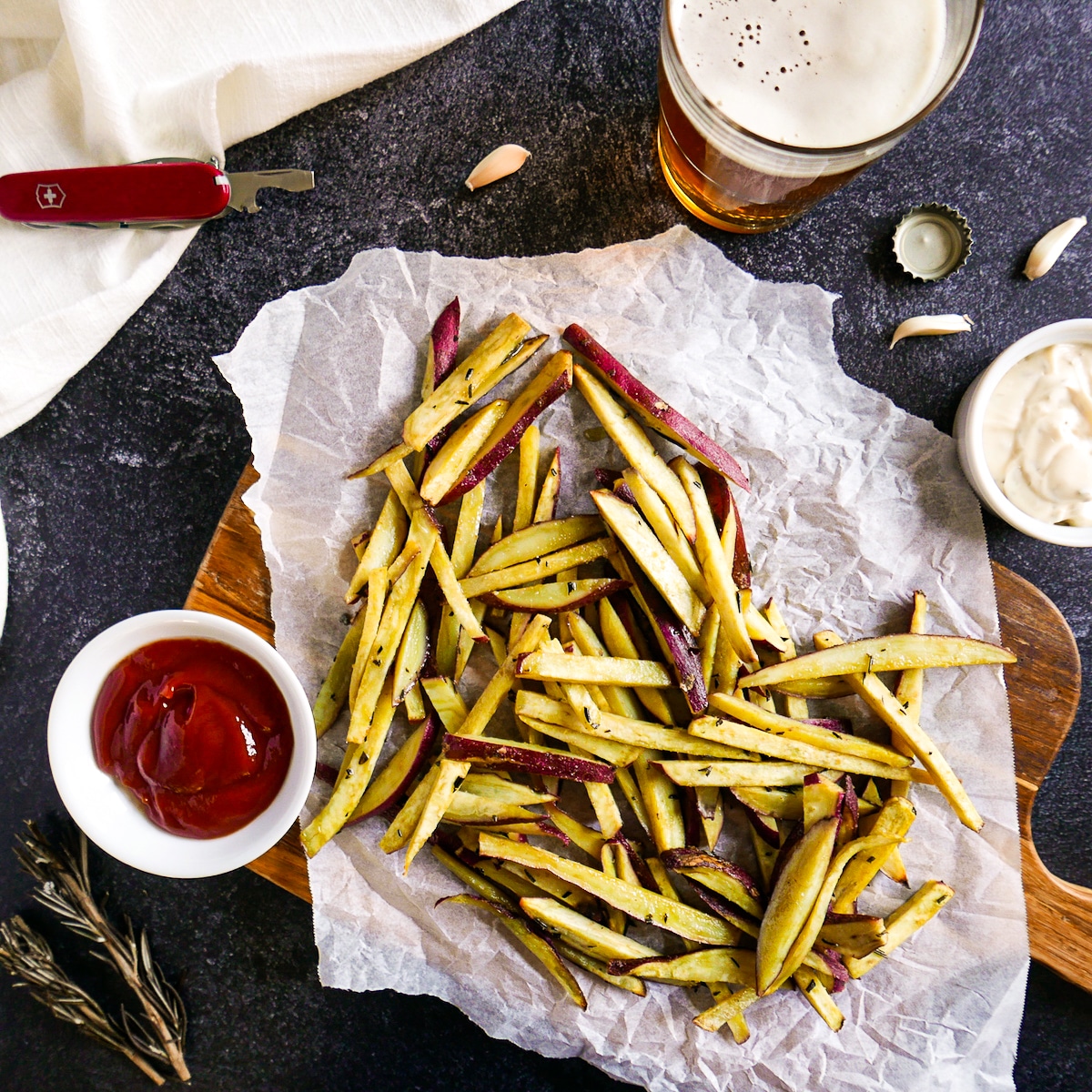 Roasted japanese sweet potato fries on a wooden cutting board with beer and condiments.