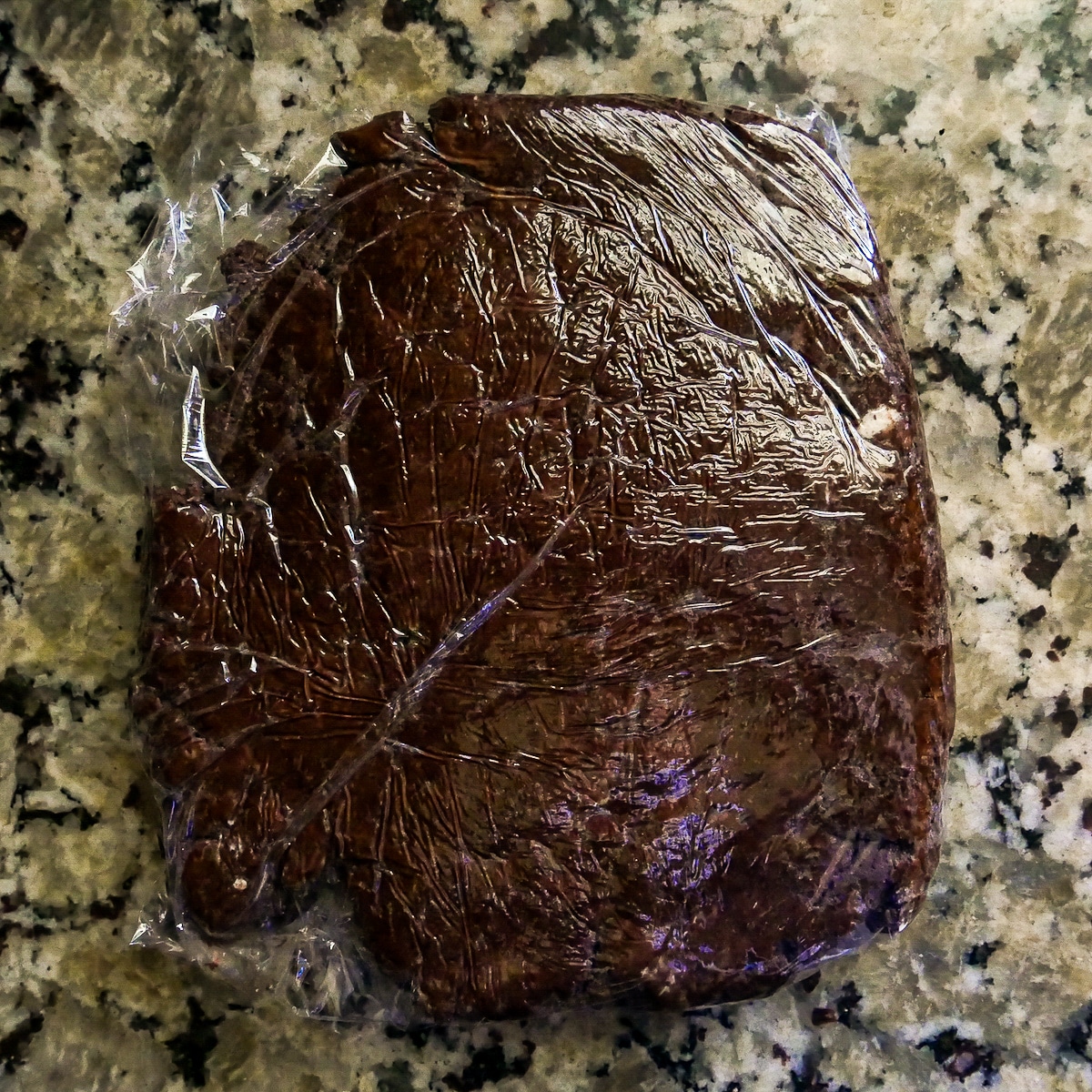 Donut dough wrapped in plastic wrap on a counter.