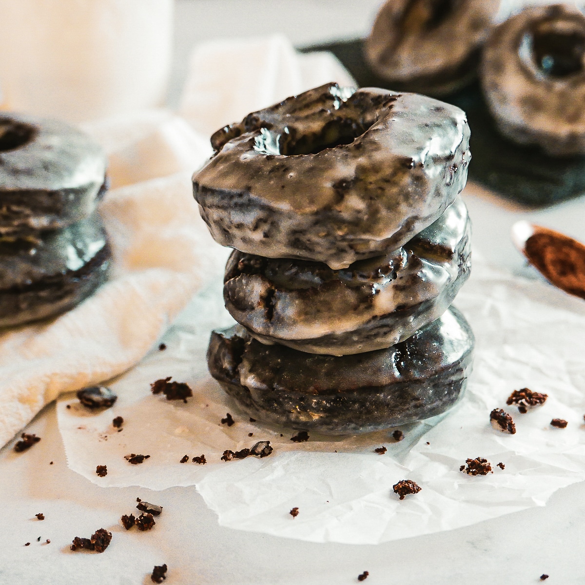 Three chocolate donuts stacked on parchment paper.