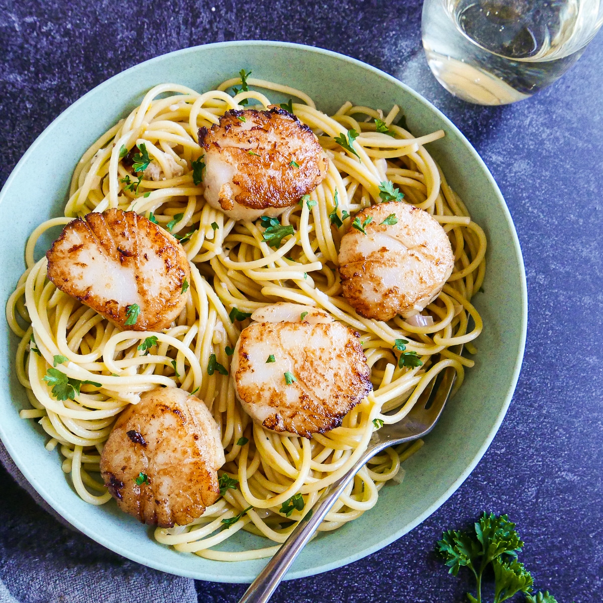 Seared scallops and pasta plated in a bowl with a fork.
