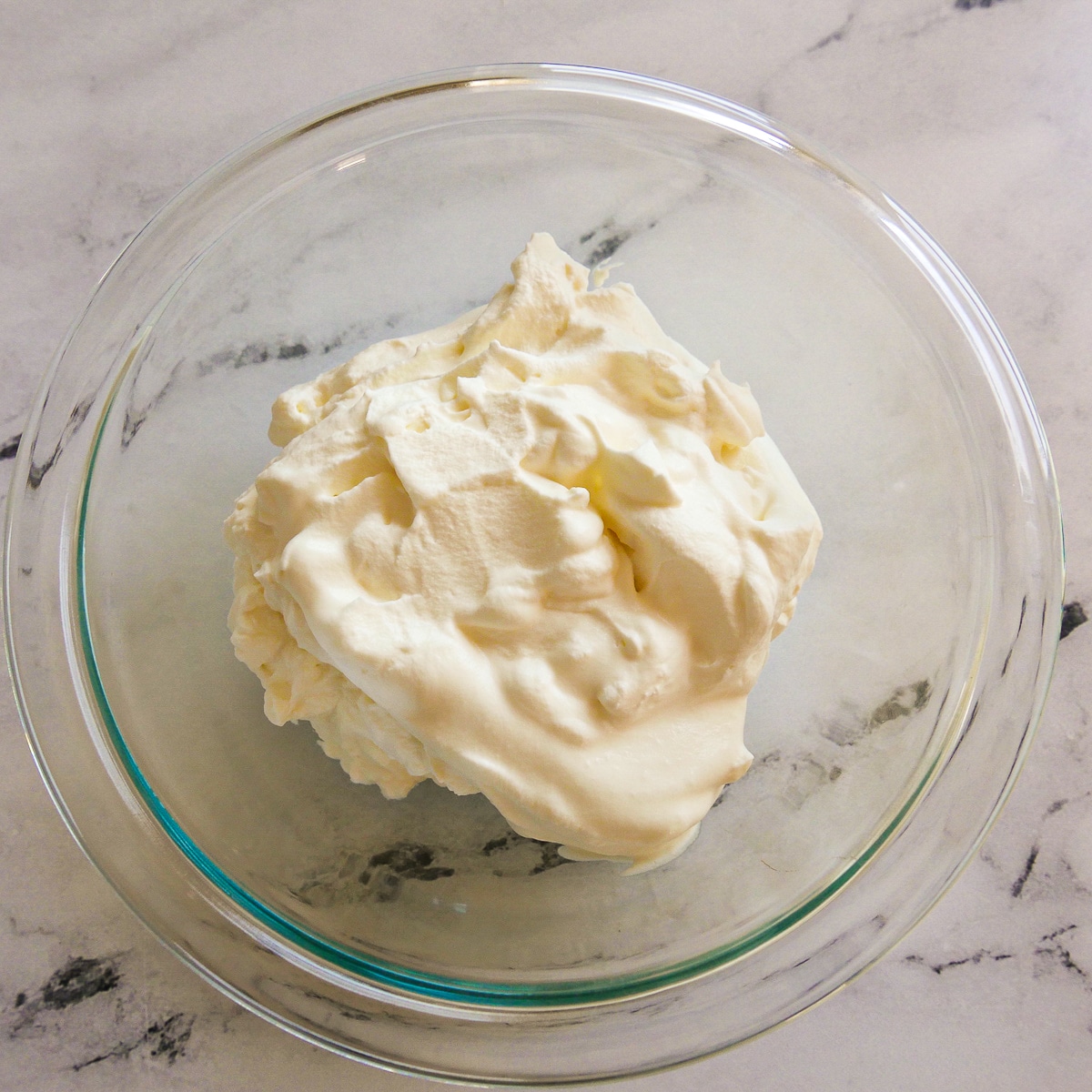 Fresh whipped cream with stiff peaks placed in a mixing bowl.