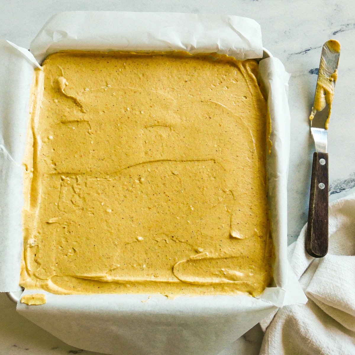 Cheesecake filling spread on top of gingersnap crust in a square pan.