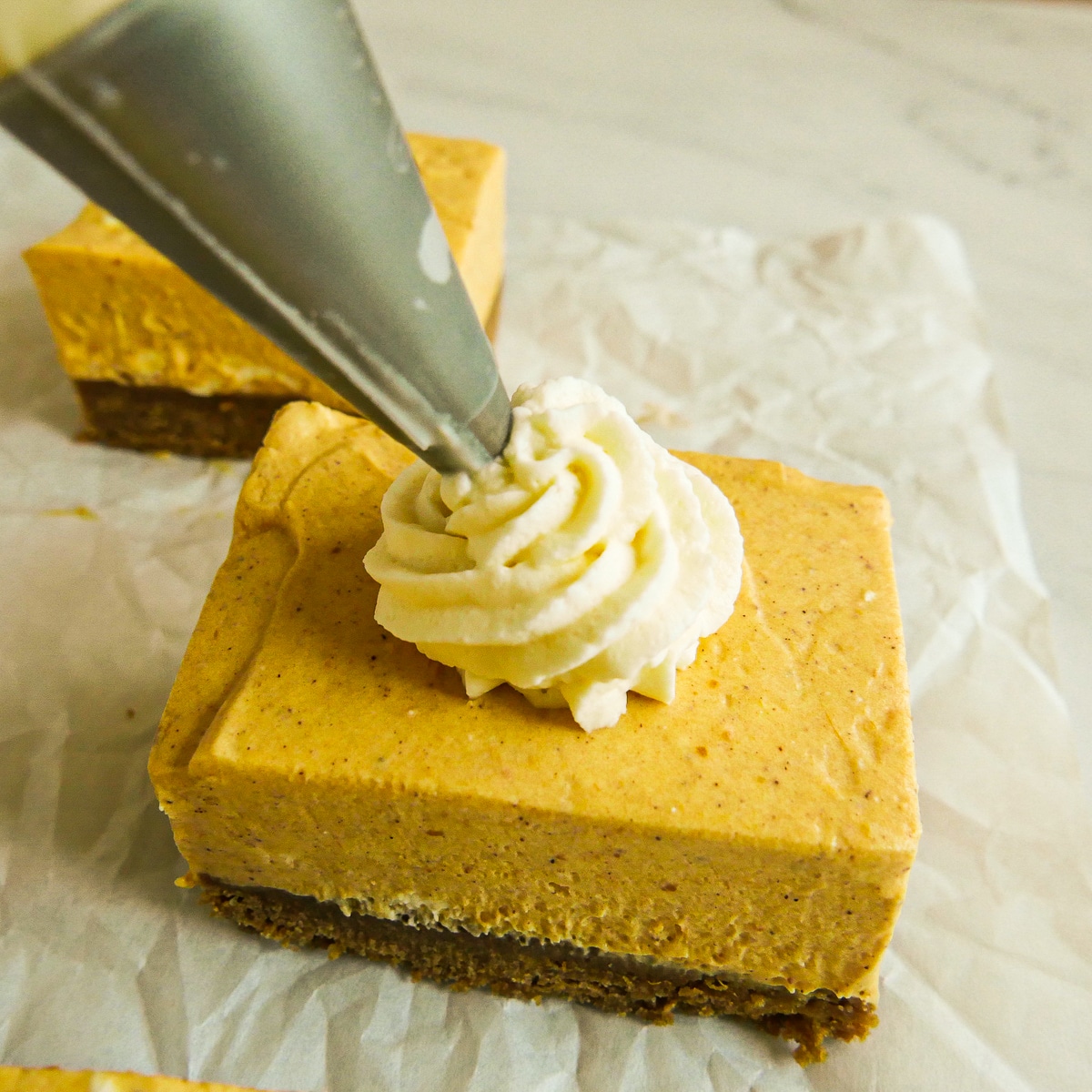 Piping swirls on top of no bake cheesecake bars using a pastry bag.