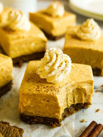 Creamy pumpkin cheesecake bars topped with whipped cream and arranged on parchment paper.