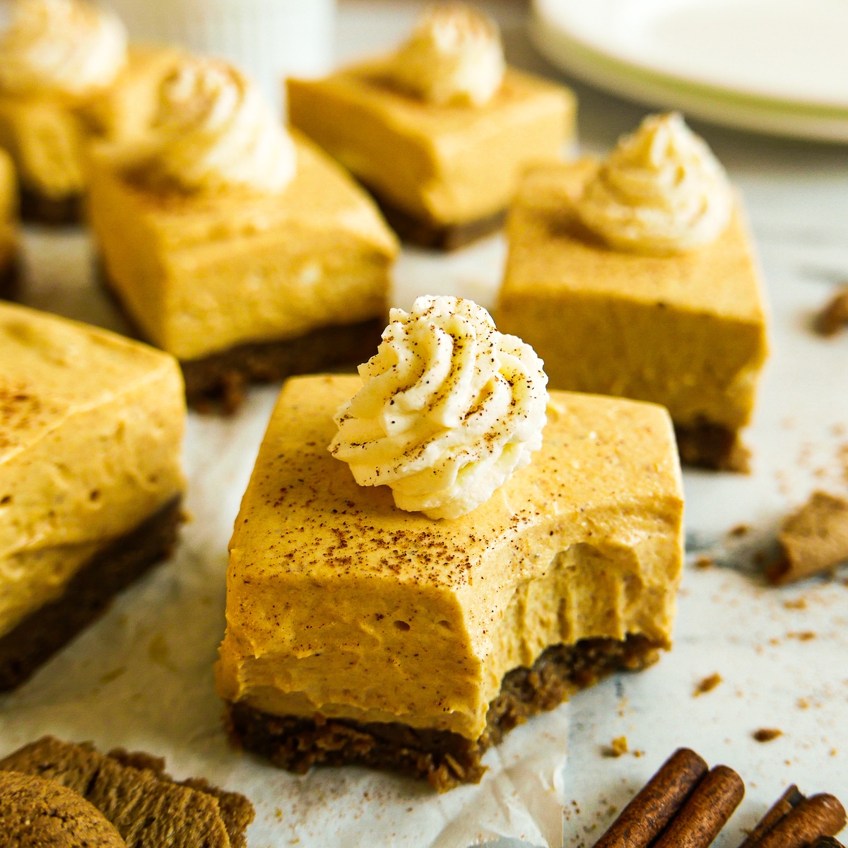 Creamy pumpkin cheesecake bars topped with whipped cream and arranged on parchment paper.