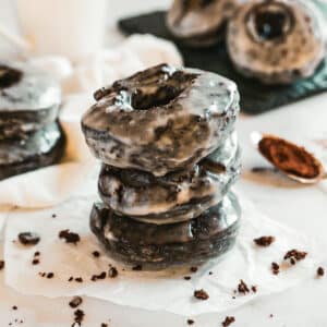 stack of three old fashioned chocolate donuts with more donuts in the background.