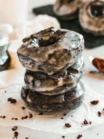 stack of three old fashioned chocolate donuts with more donuts in the background.