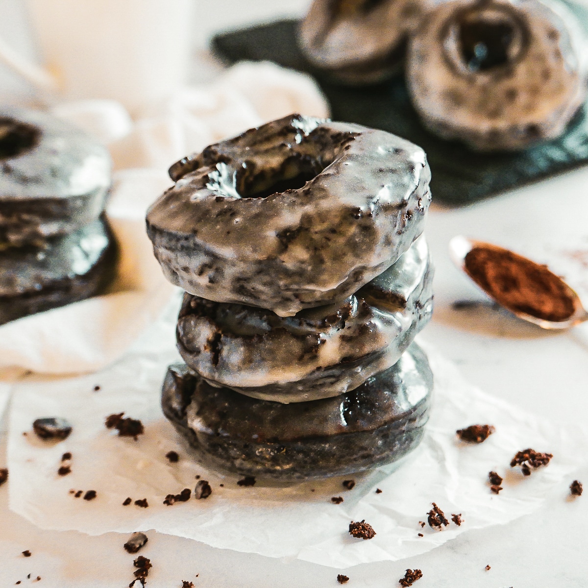 donuts-stacked.jpg stack of three old fashioned chocolate donuts with more donuts in the background.