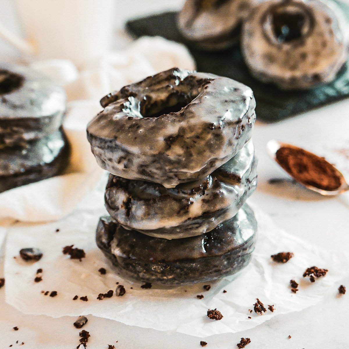 stack of three old fashioned chocolate donuts with more donuts in the background.