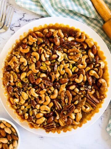 Mixed nut tart on a white platter with gingham napkin and rolling pin.