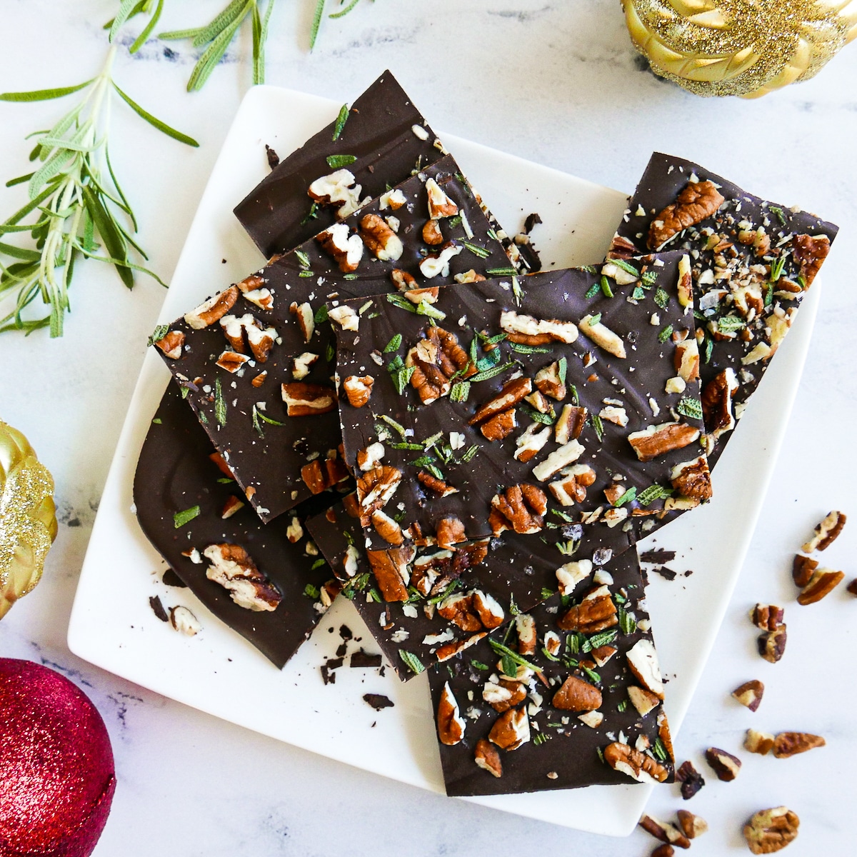 Chocolate bark topped with pecans and rosemary on a plate.