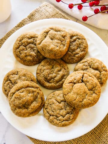 plate of chewy ginger snap cookies with red holly in the background.