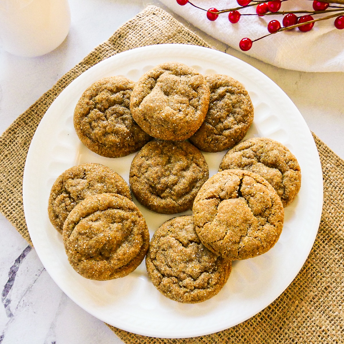 plate of chewy ginger snap cookies with red holly in the background.