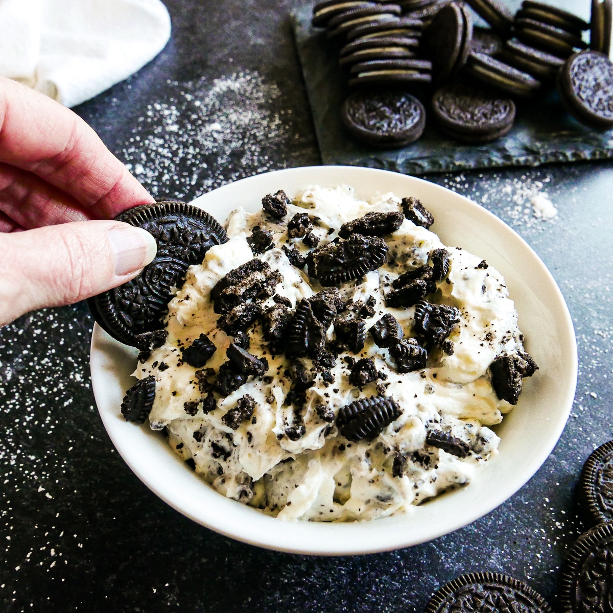 Hand dipping an oreo into sweet oreo cream dip.