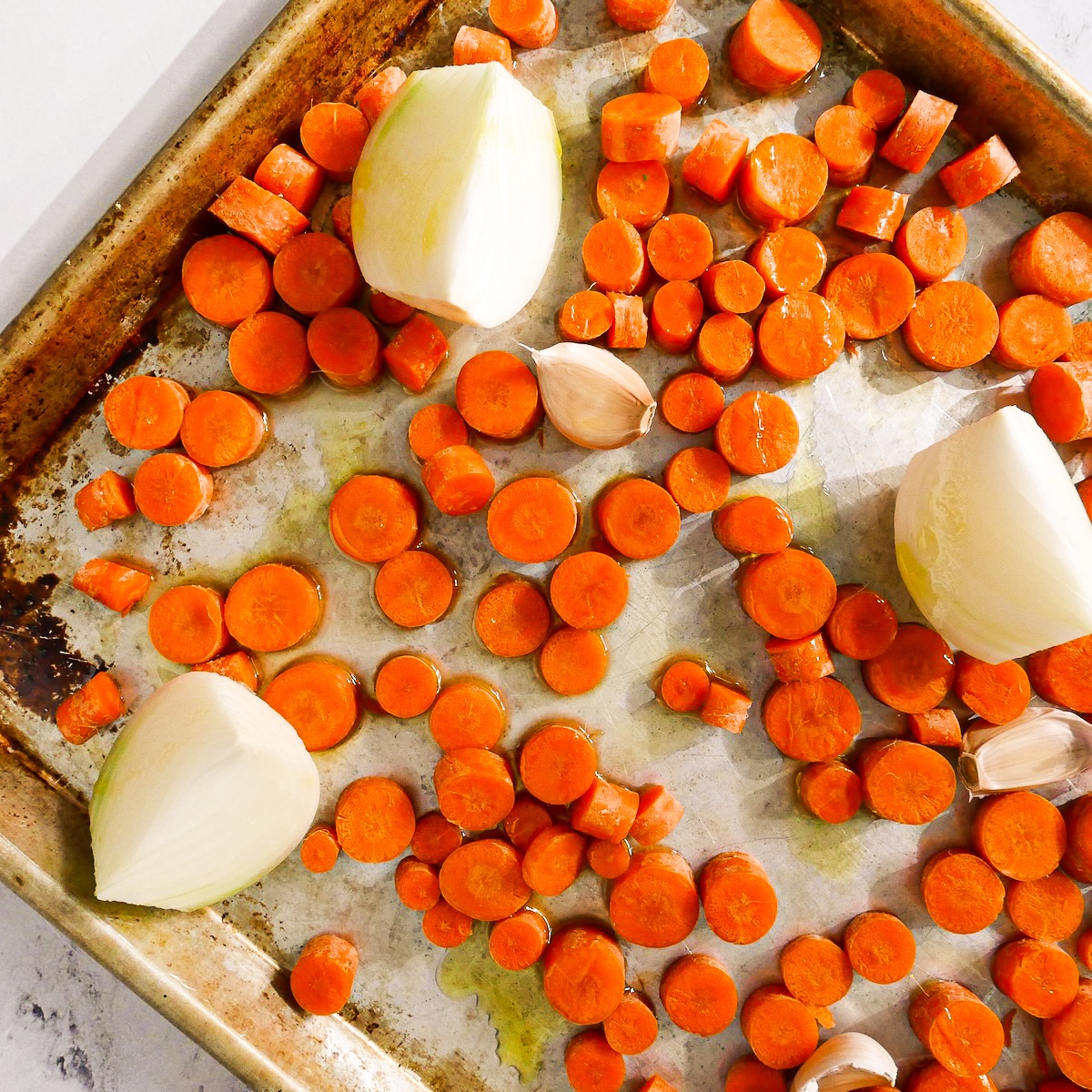 Sliced carrots, onions, and garlic on a baking sheet.