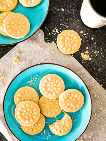 Aromatic cardamom shortbread cookies arranged on two blue plates with a cup of coffee.